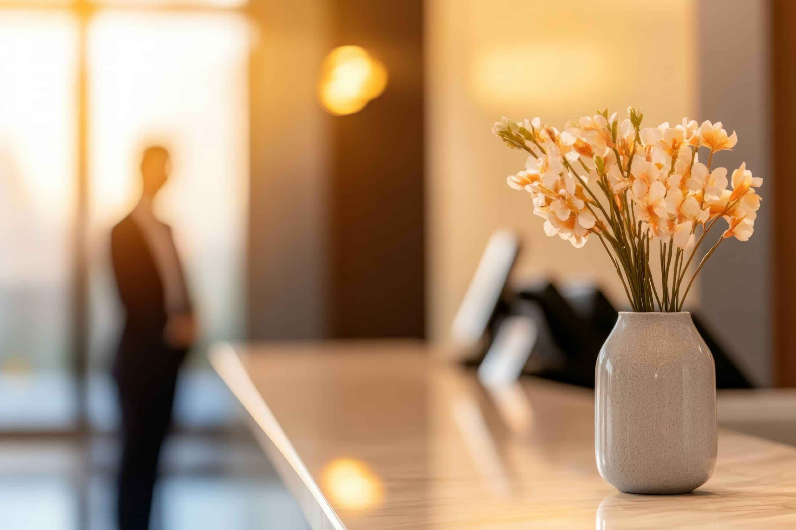 Blumentopf als Blickfang auf dem Tresen eines Empfangsbereichs in warmer Lichtstimmung, mit stilvoller Atmosphäre und dezenter Dekoration.