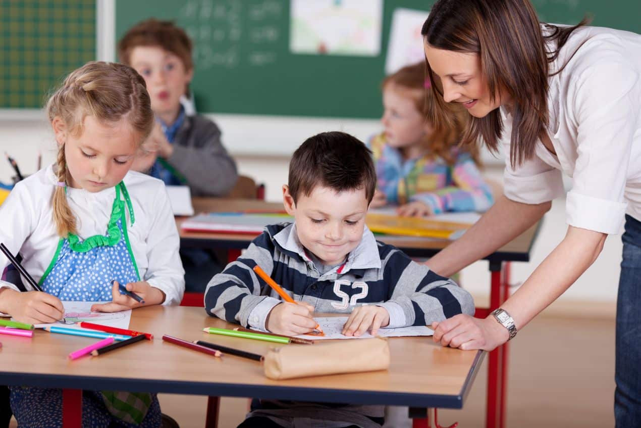 grundschule berlin: lehrerin unterstützt zwei kinder beim schreiben und malen – förderung im kreativen grundschulunterricht